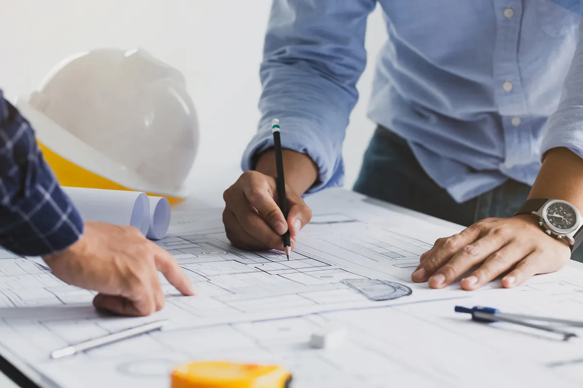 Zwei Bauleiter besprechen sich. Auf einem Tisch zwischen Ihnen liegen Pläne und Grundrisse